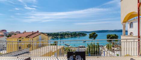 A balcony with a table set for two, overlooking a body of water and a coastal town.