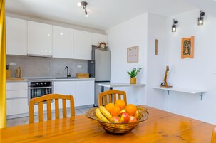 Una cocina moderna con armarios blancos, un refrigerador y una mesa de comedor con un frutero.