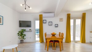 A modern living room with a wooden dining table, yellow curtains, a flat-screen TV, and a potted plant. - Apartment Rizza (Trogir)