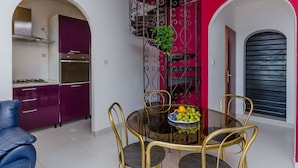 A compact kitchen with modern appliances, a dining area with a glass table and metal chairs, and a staircase with a decorative railing. - House Zdenka (Okrug Donji)