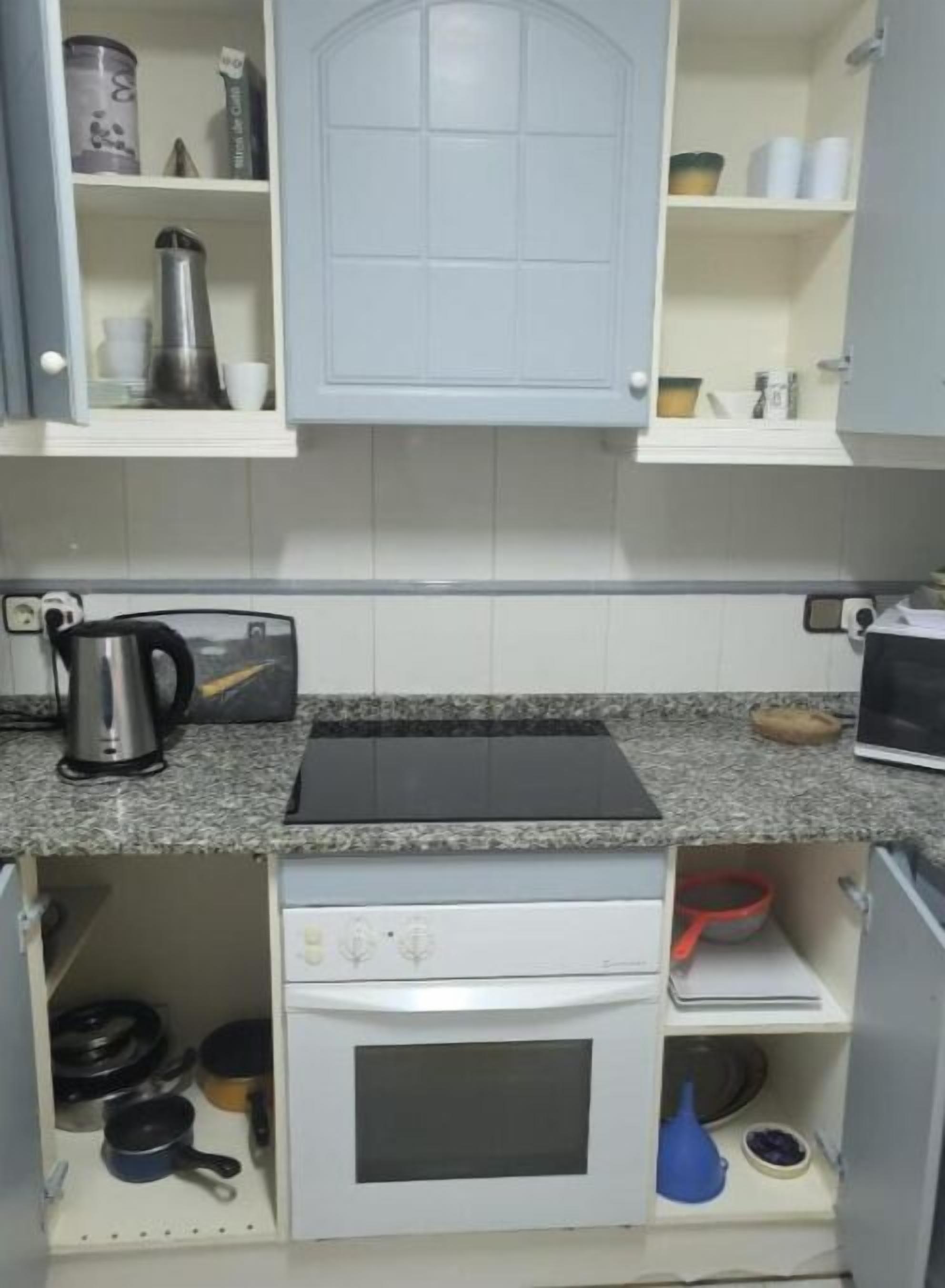Una cucina compatta con forno integrato, una macchina per il caffè e diversi utensili da cucina.