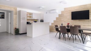 A modern kitchen with white cabinets, a central island, and a dining area with a table and chairs. - Apartments Sky (Trogir)