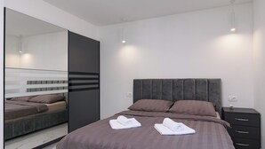 A modern bedroom with a large bed, a dark headboard, a bedside table, and a mirror. - Apartments Sky (Trogir)