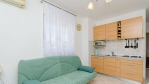 A living room with a green sofa and a kitchen area with wooden cabinets and a microwave. - Apartment Mario (Okrug Gornji)
