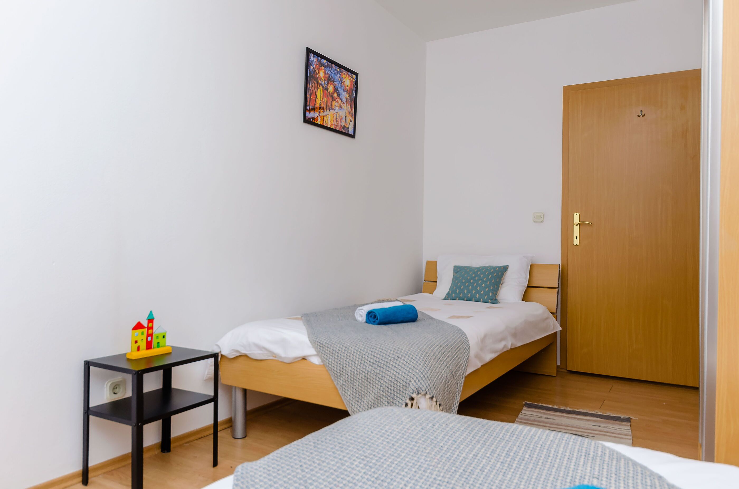 Ein Schlafzimmer mit einem Bett, einem kleinen Tisch mit Spielzeug, einer Tür und einem Bild an der Wand.