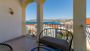 A balcony with a view of a coastal town, a chair, and a small potted plant. - Apartment Mario (Okrug Gornji)