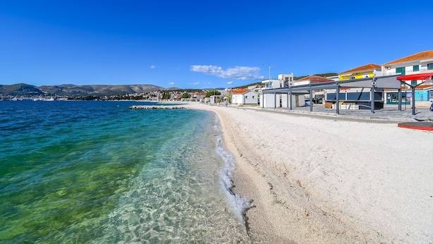 A beach with clear water, a sandy shore, and buildings with signage. - Apartment Mario (Okrug Gornji)