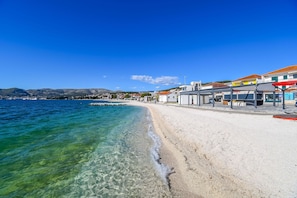 A beach with clear water, a sandy shore, and buildings with signage. - Apartment Mario (Okrug Gornji)