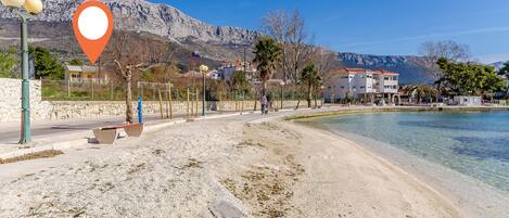 A beach with a clear view of the sea, a stone wall, and buildings in the background.