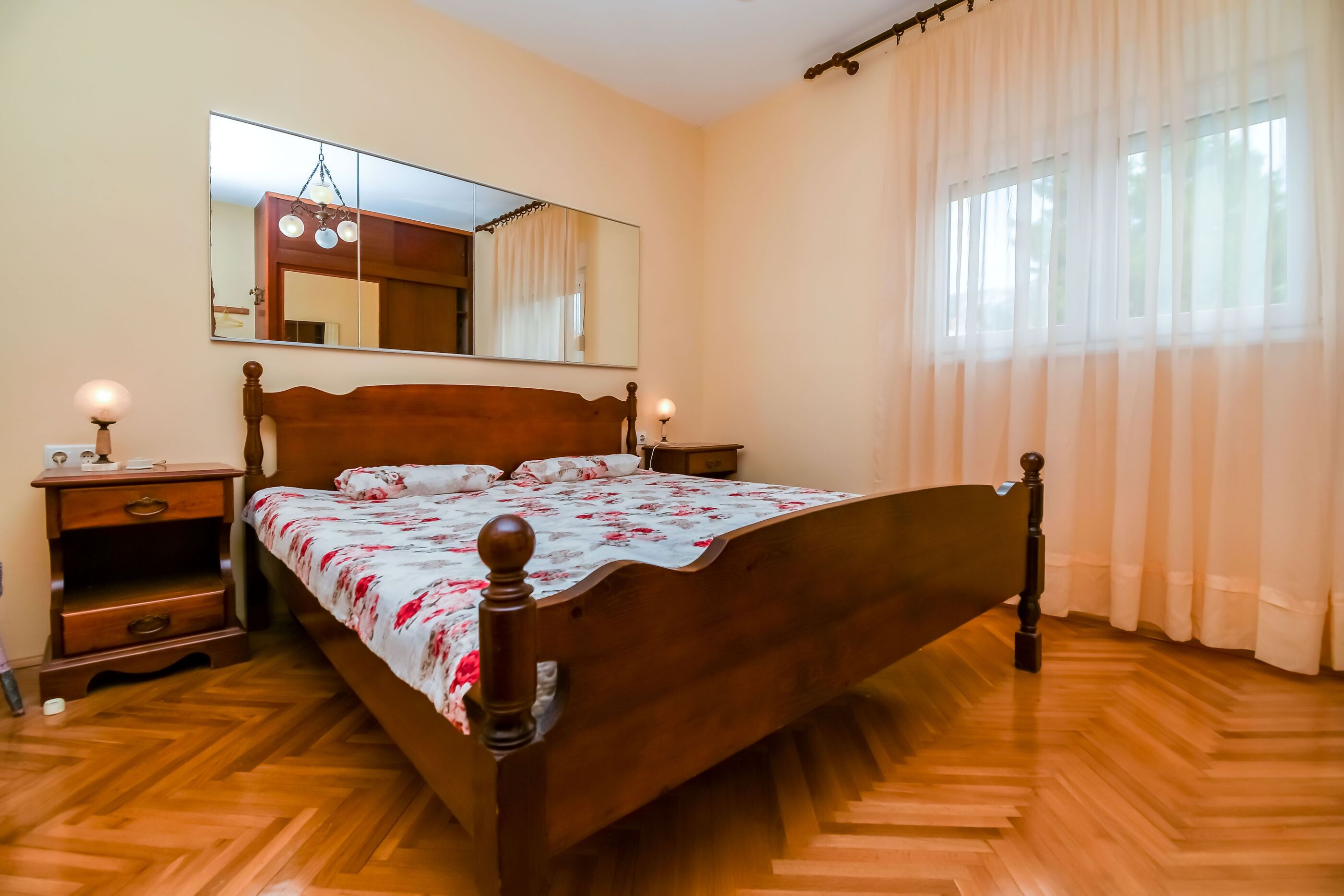 Un dormitorio con cama de madera, mesita de noche, cómoda, espejo y ventana con cortinas.