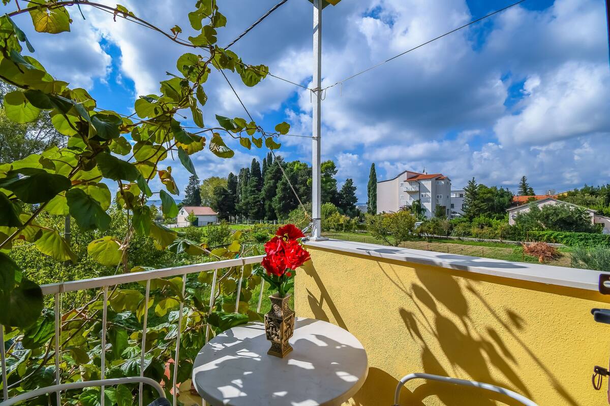 A balcony with a white table, a vase with red flowers, and a yellow wall.