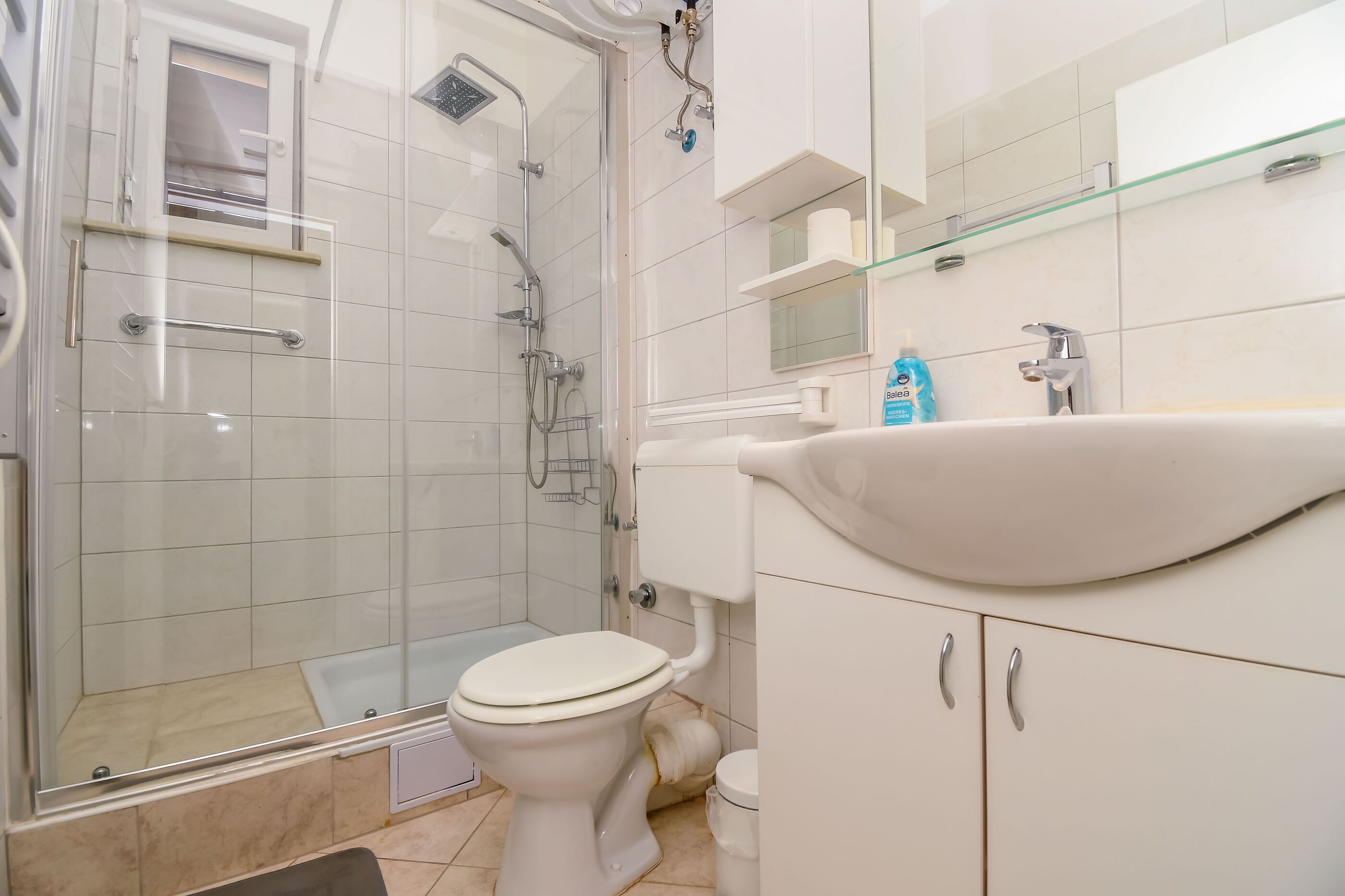 A bathroom with a glass-enclosed shower, a toilet, a sink, and a mirror.