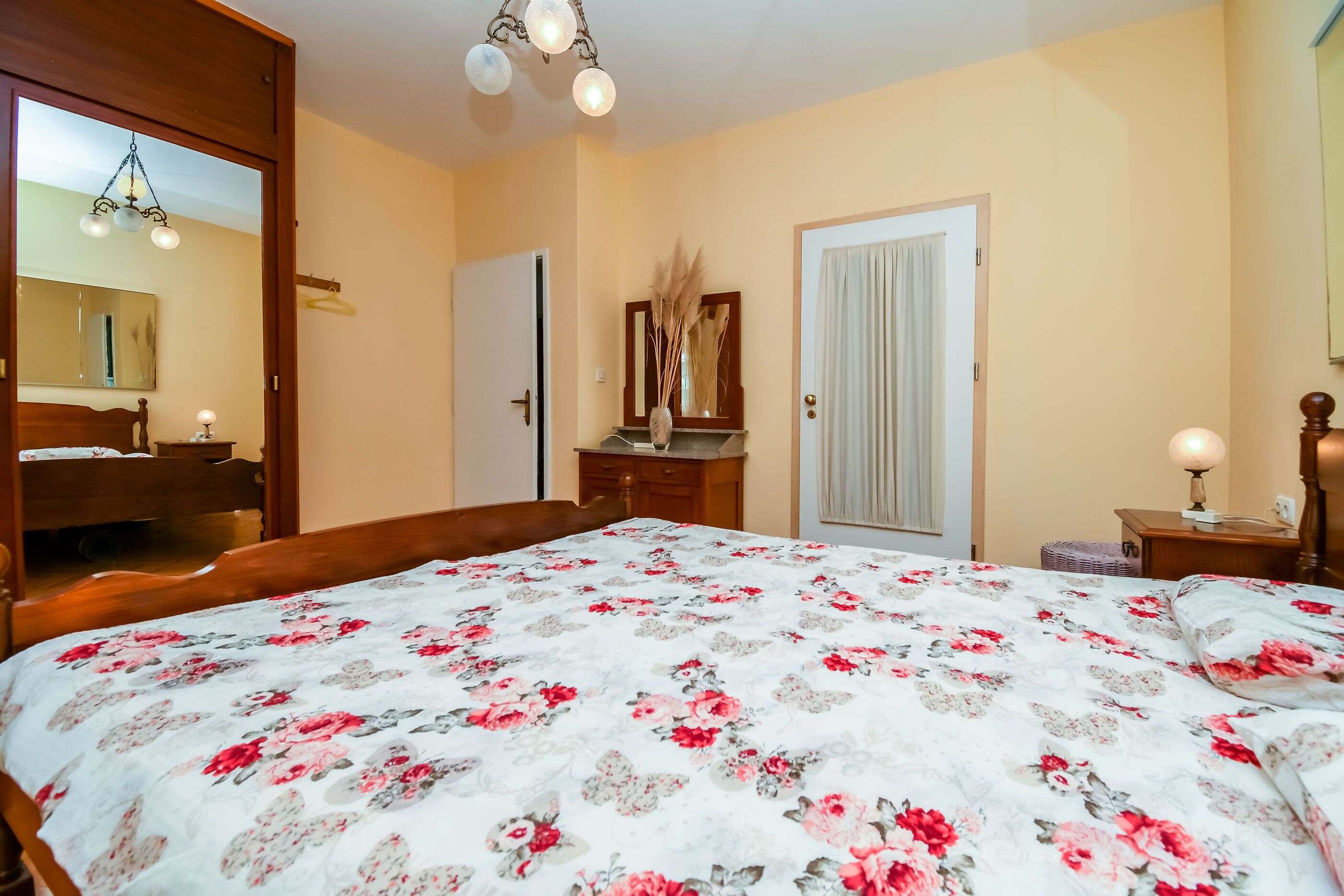 Quarto com cama grande, cômoda, espelho e porta.