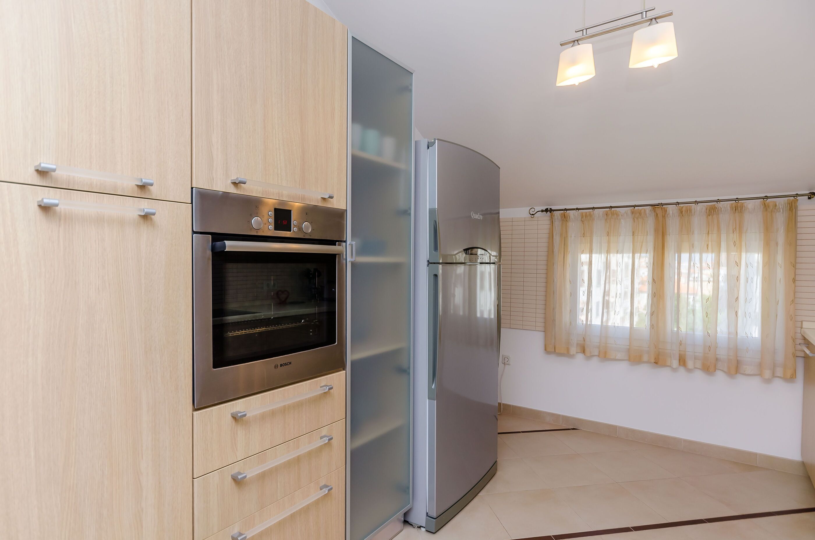 A kitchen with a Bosch oven, a stainless steel refrigerator, and light wooden cabinets.