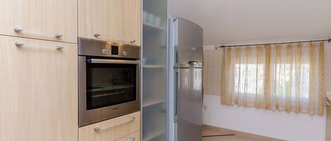 A kitchen with a Bosch oven, a stainless steel refrigerator, and light wooden cabinets.