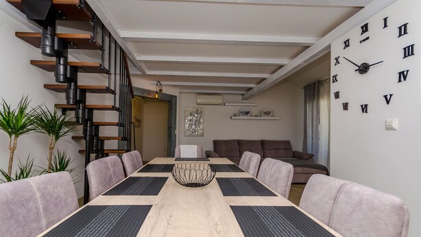 A modern dining area with a long table, cushioned chairs, a decorative centerpiece, and a staircase. - Apartment Dora (Trogir)