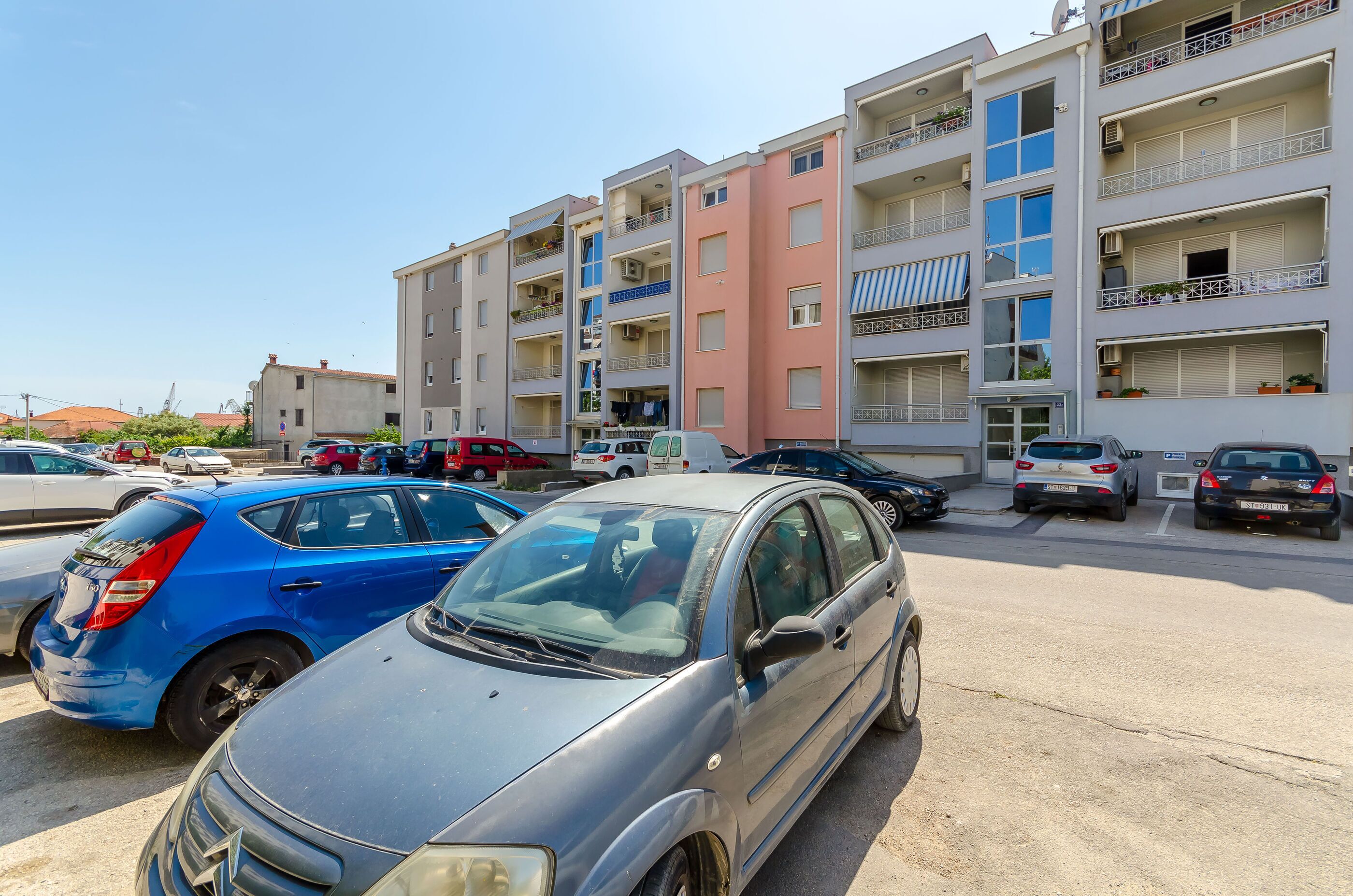 A parking lot with several cars parked in front of a multi-story residential building with balconies.