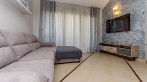 A modern living room with a sectional sofa, a TV mounted on a textured wall, and a wooden console table. - Apartment Dora (Trogir)
