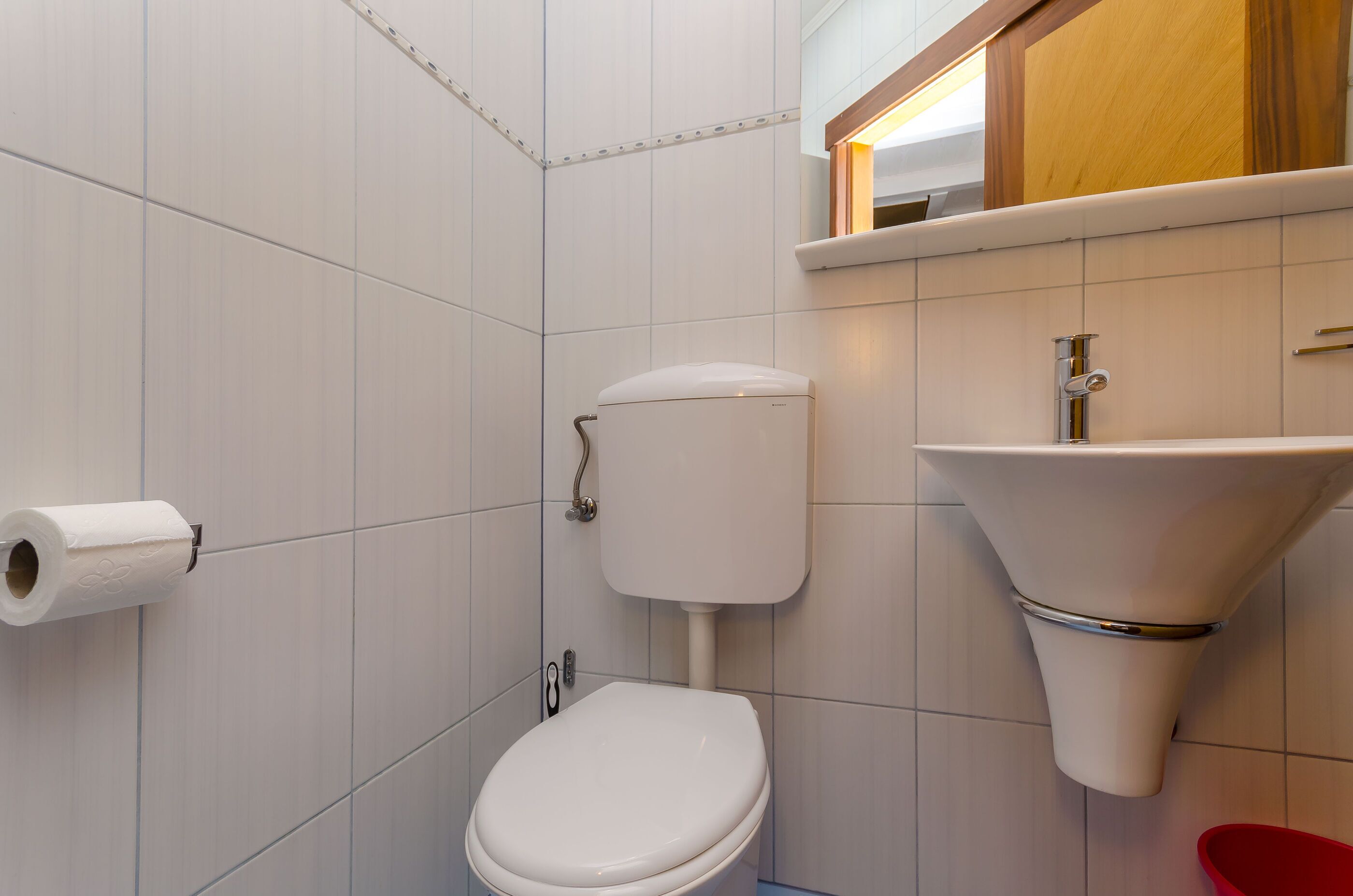 A bathroom with a toilet, a sink, and a roll of toilet paper on the wall.