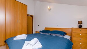 A bedroom with a large wooden wardrobe, a bed with blue bedding, and a nightstand with a lamp. - Apartment Dora (Trogir)