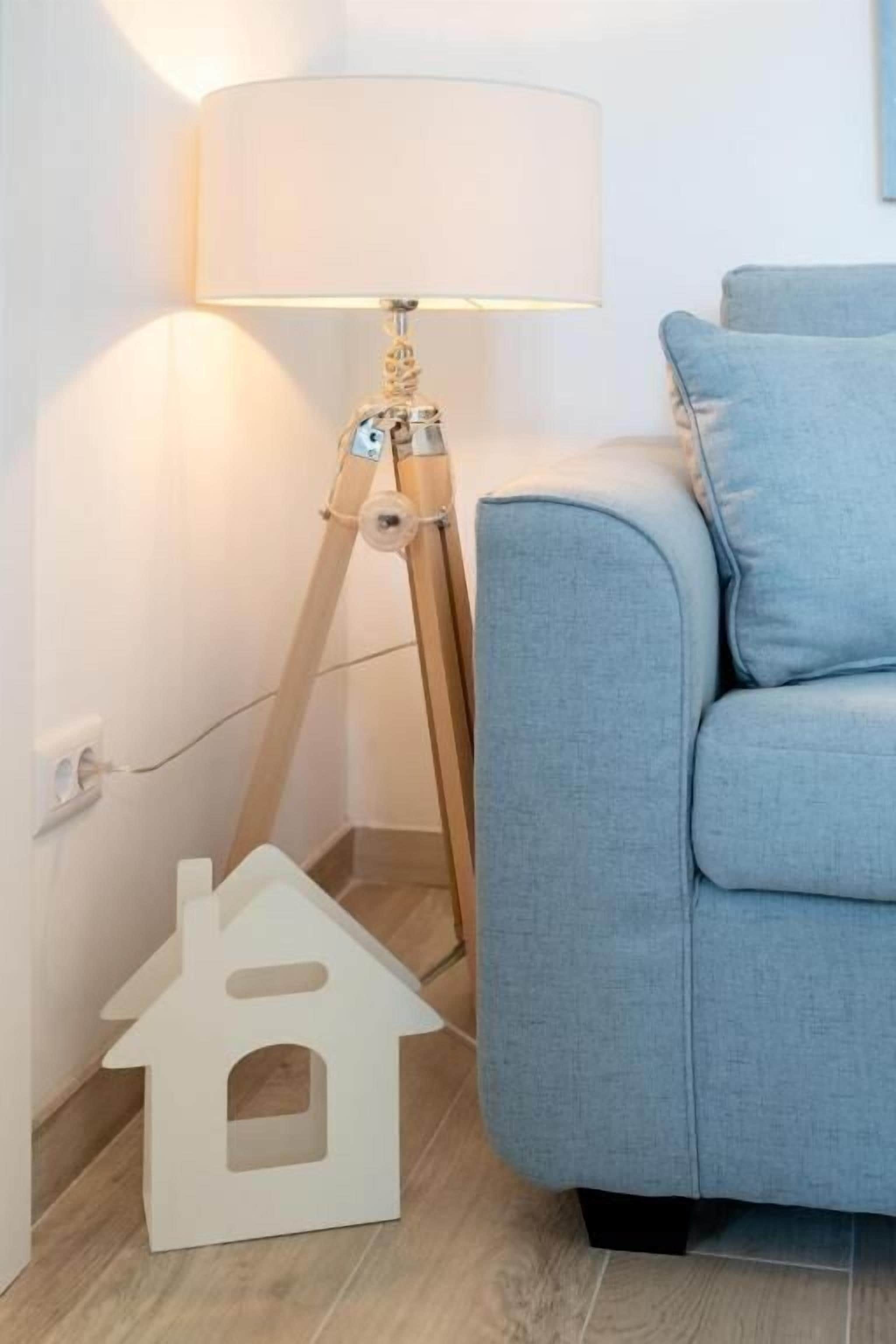 A room with a light blue sofa, a floor lamp, and a white house-shaped object on the floor.