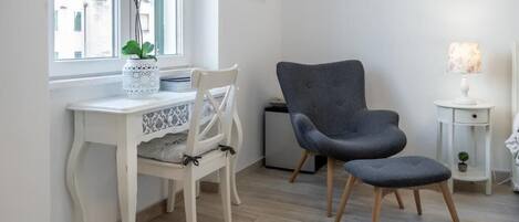 A modern room with a white desk, a grey armchair, and a small side table with a lamp.