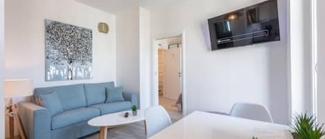 En moderne stue med en blå sofa, et hvidt sofabord og et fladskærms-tv monteret på væggen.