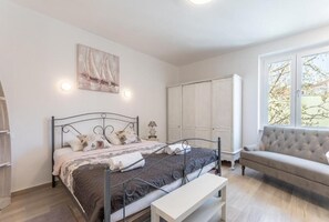 A bedroom with a bed, a bench, a sofa, a wardrobe, and a painting on the wall. - Apartments and Room Poesia (Split)
