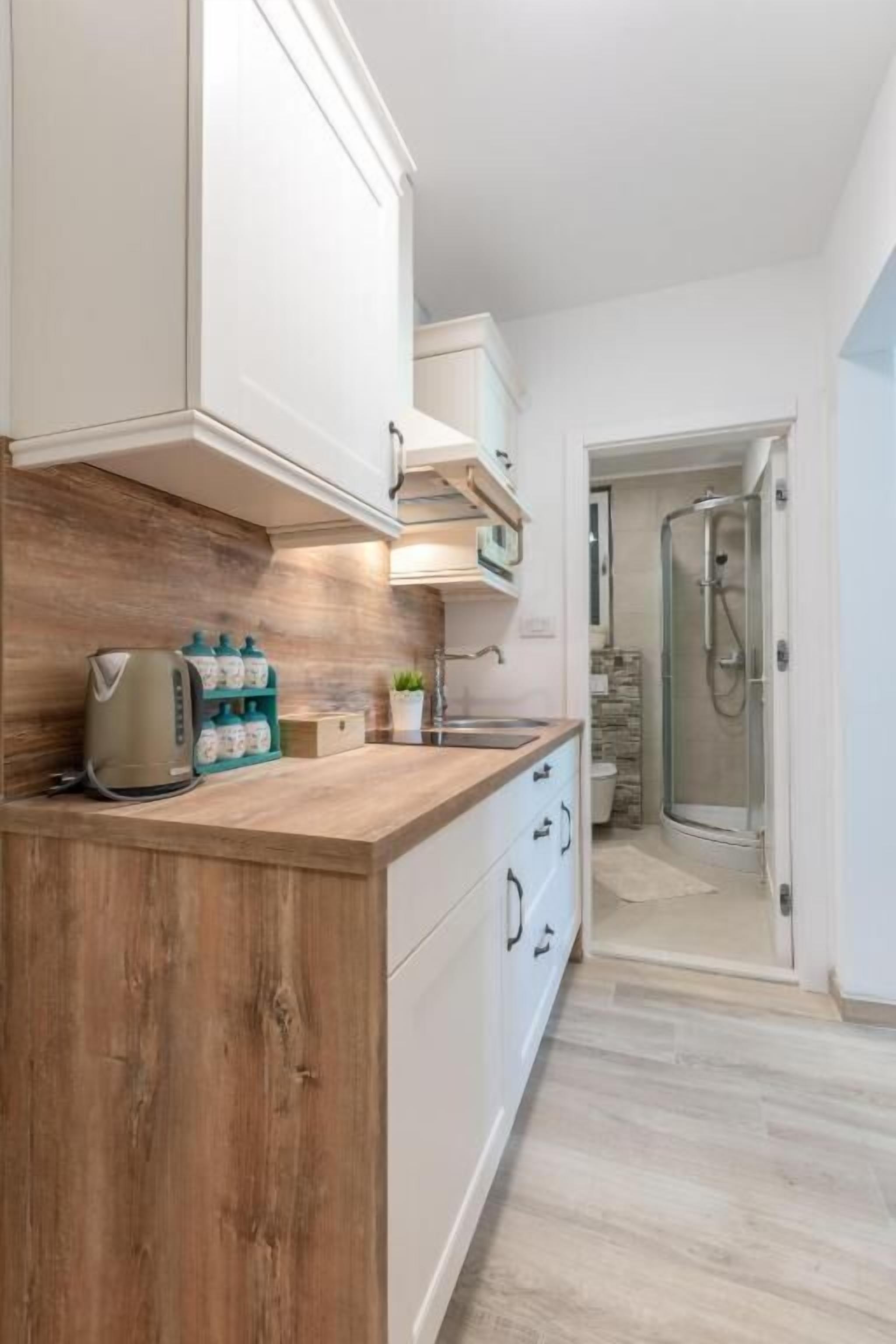 A modern kitchen with wooden countertops, white cabinets, and a built-in oven. A coffee maker and storage containers are visible on the counter.