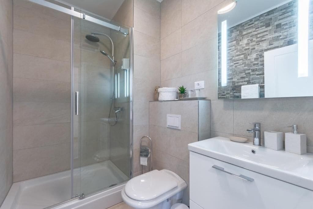 Une salle de bain moderne avec une douche à parois de verre, des toilettes blanches et un meuble-lavabo avec un miroir.