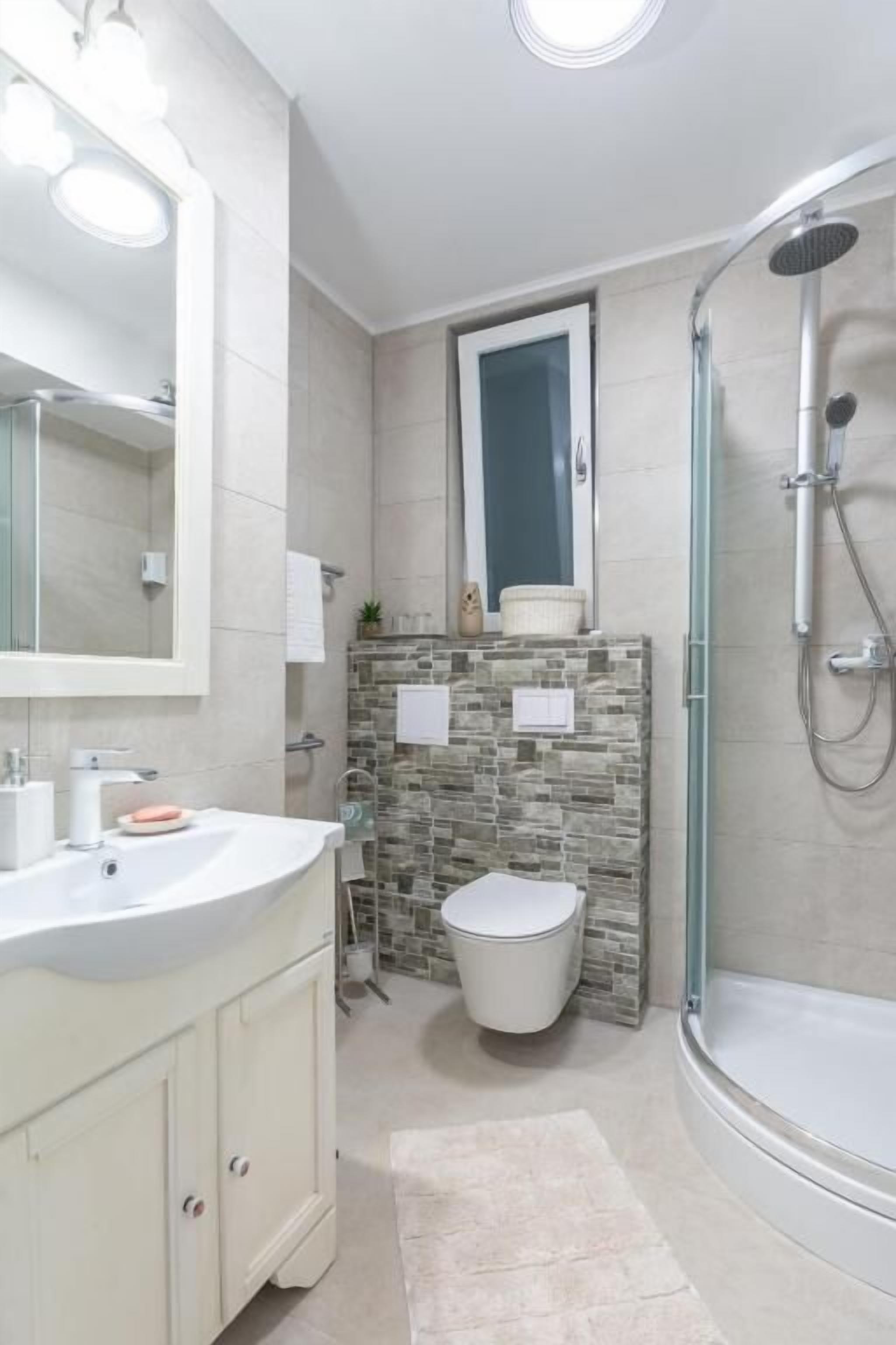 Ein modernes Badezimmer mit einer Duschwanne, einem großen Spiegel und einer Wand mit Natursteinverkleidung.