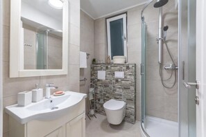 A modern bathroom with a glass-enclosed shower, a white sink with a marble countertop, and a tiled backsplash. - Apartments and Room Poesia (Split)