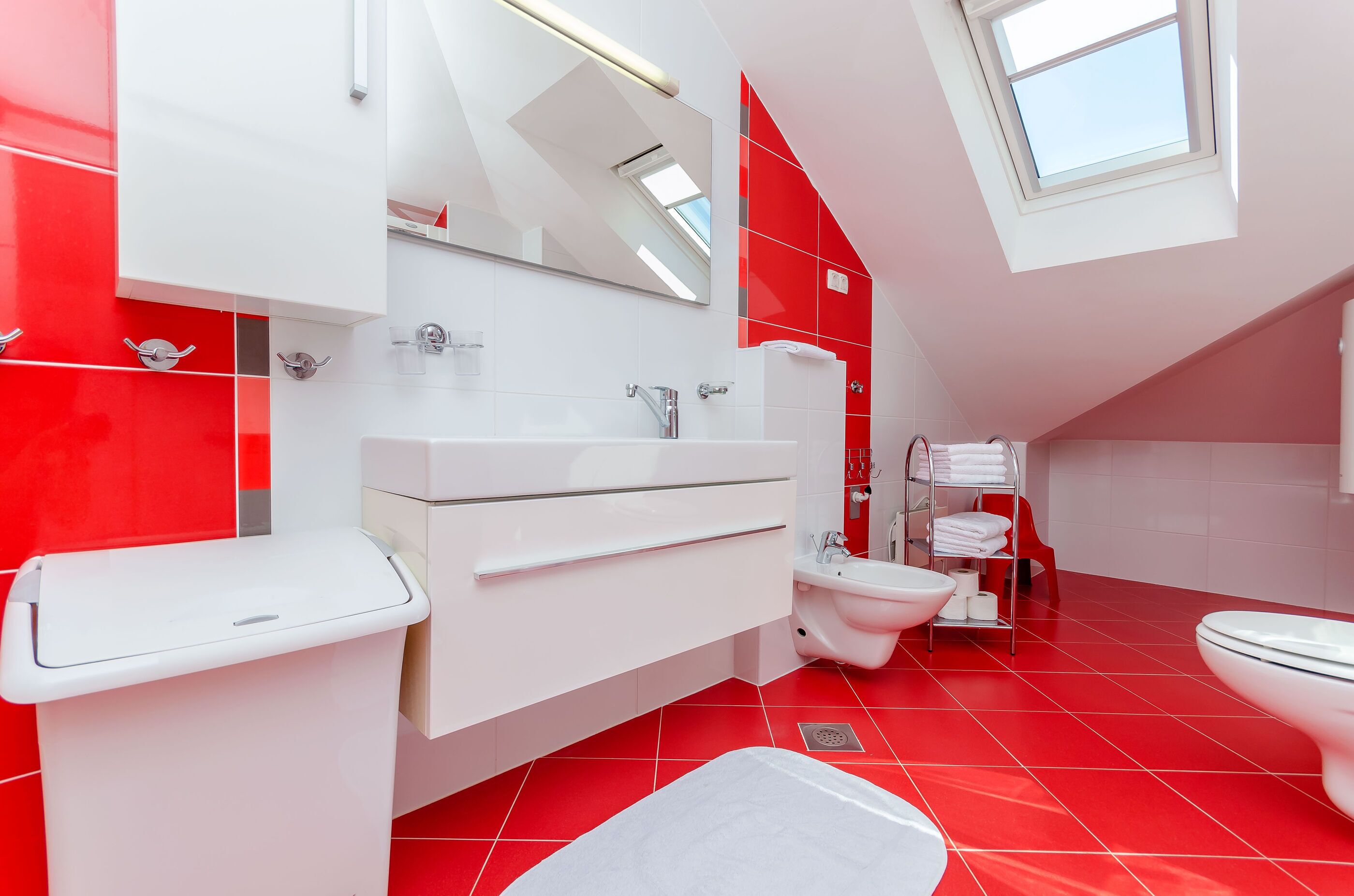 Een moderne badkamer met een kleurenschema van rood en wit, een dakraam en een witte wastafel met een wastafel en spiegel.
