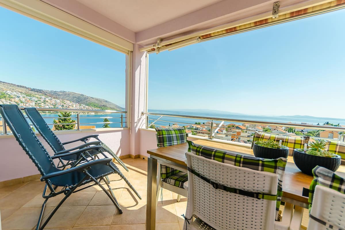 Een balkon met uitzicht op zee, een tafel met stoelen en potplanten.