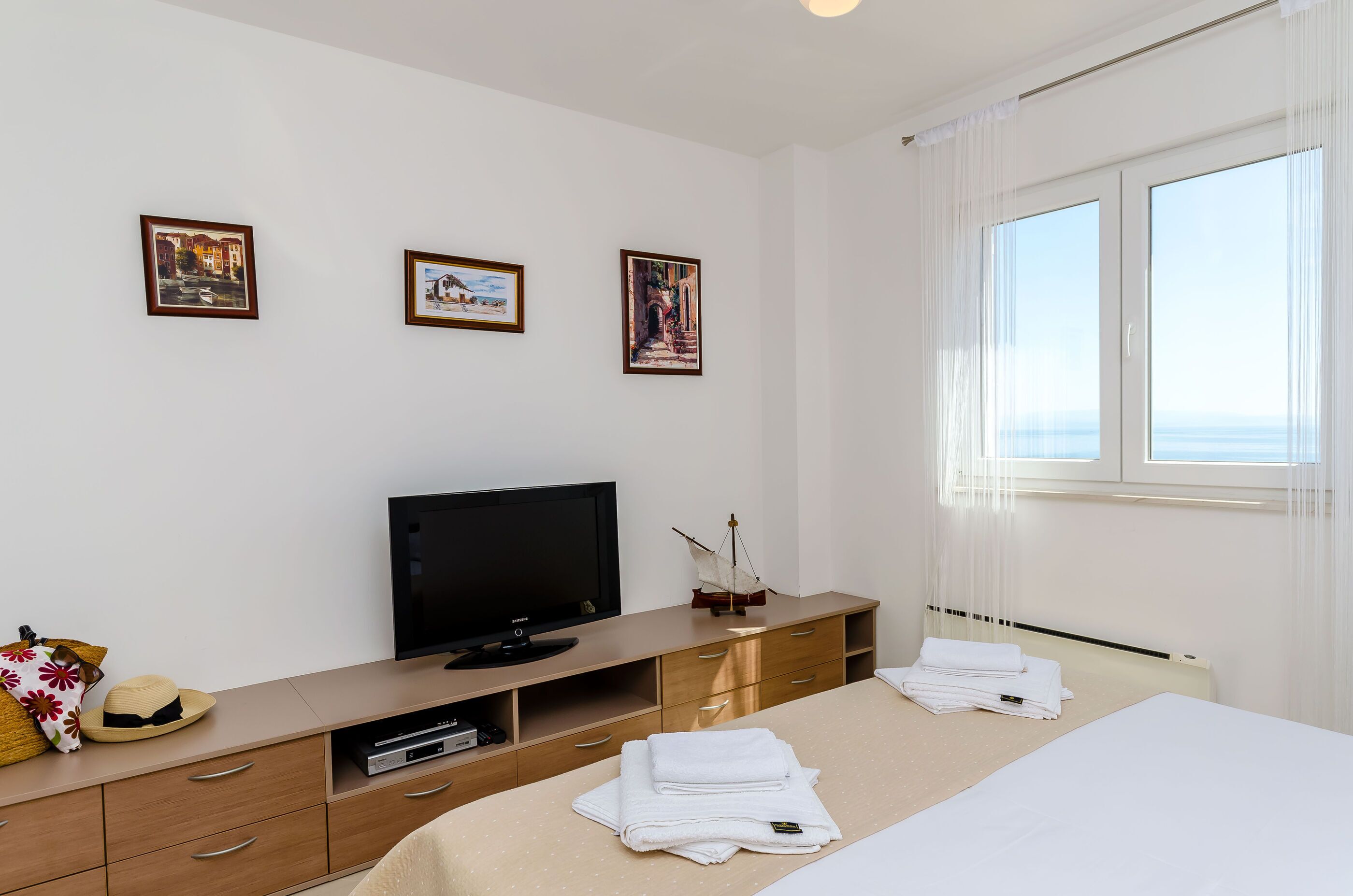 A hotel room with a bed, a television, a desk with a computer, and three framed pictures on the wall.