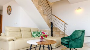 Een moderne woonkamer met een bank, een salontafel en een groene fauteuil. Achtergrond zichtbaar is een trap met een leuning.