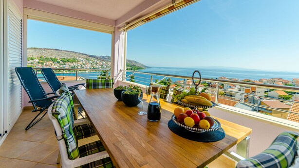 Een balkon met een houten tafel, stoelen en een schaal fruit.