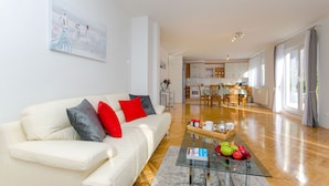 A modern living room with a white sofa, red and grey cushions, a glass coffee table with fruits, and a painting on the wall. - Apartment Gilda Lux (Split)