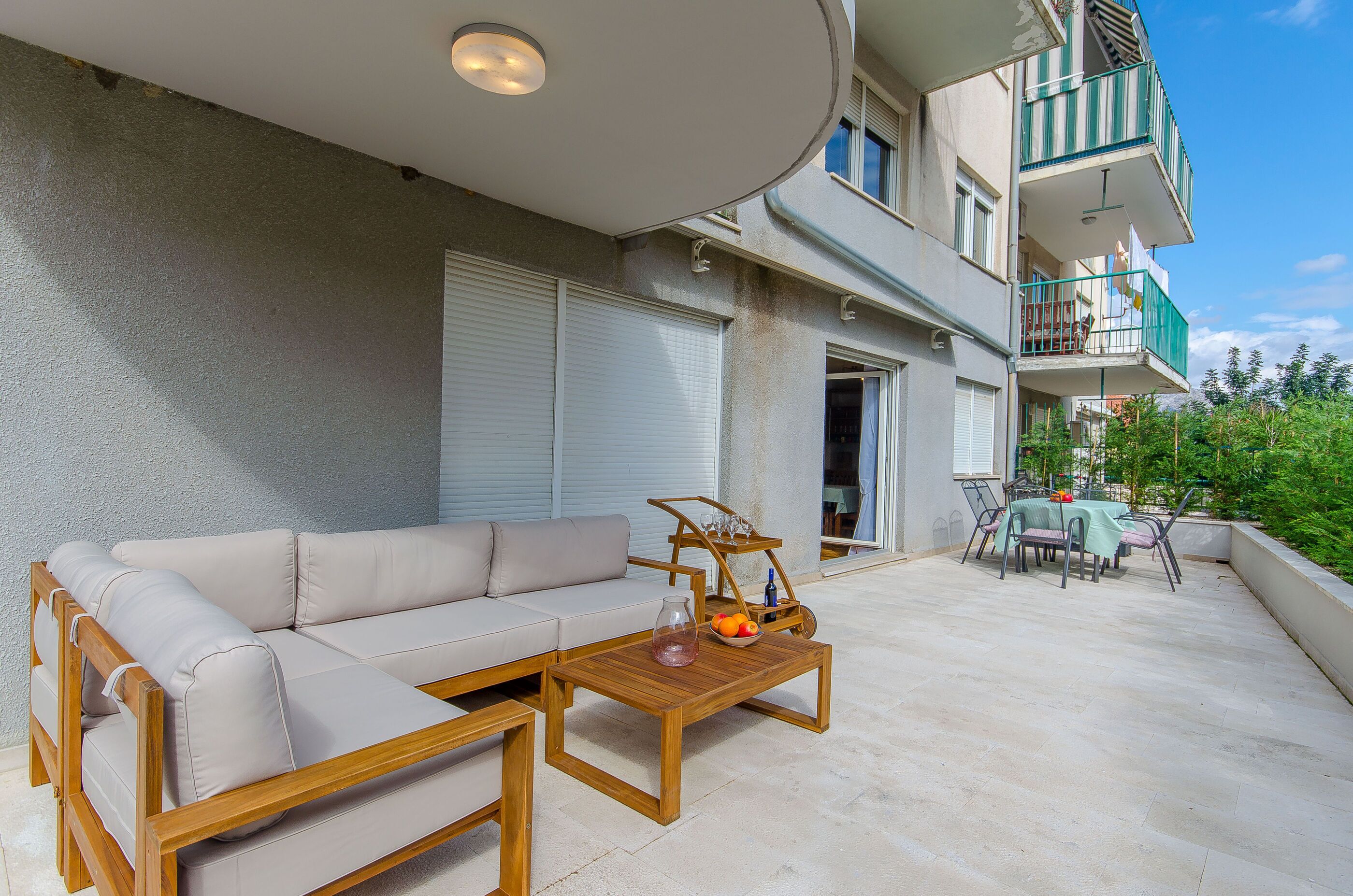 An outdoor patio with a beige sofa, wooden coffee table, and a dining table set for six.