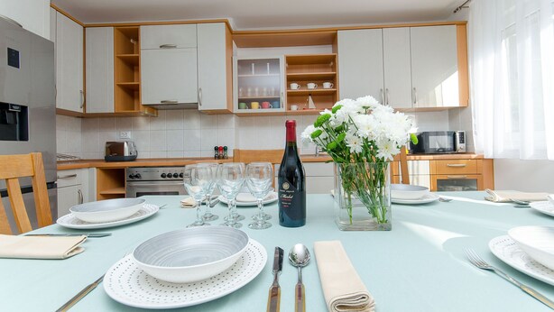 Un coin repas avec une table dressée pour quatre personnes, comprenant des assiettes, des couverts et une bouteille de vin.