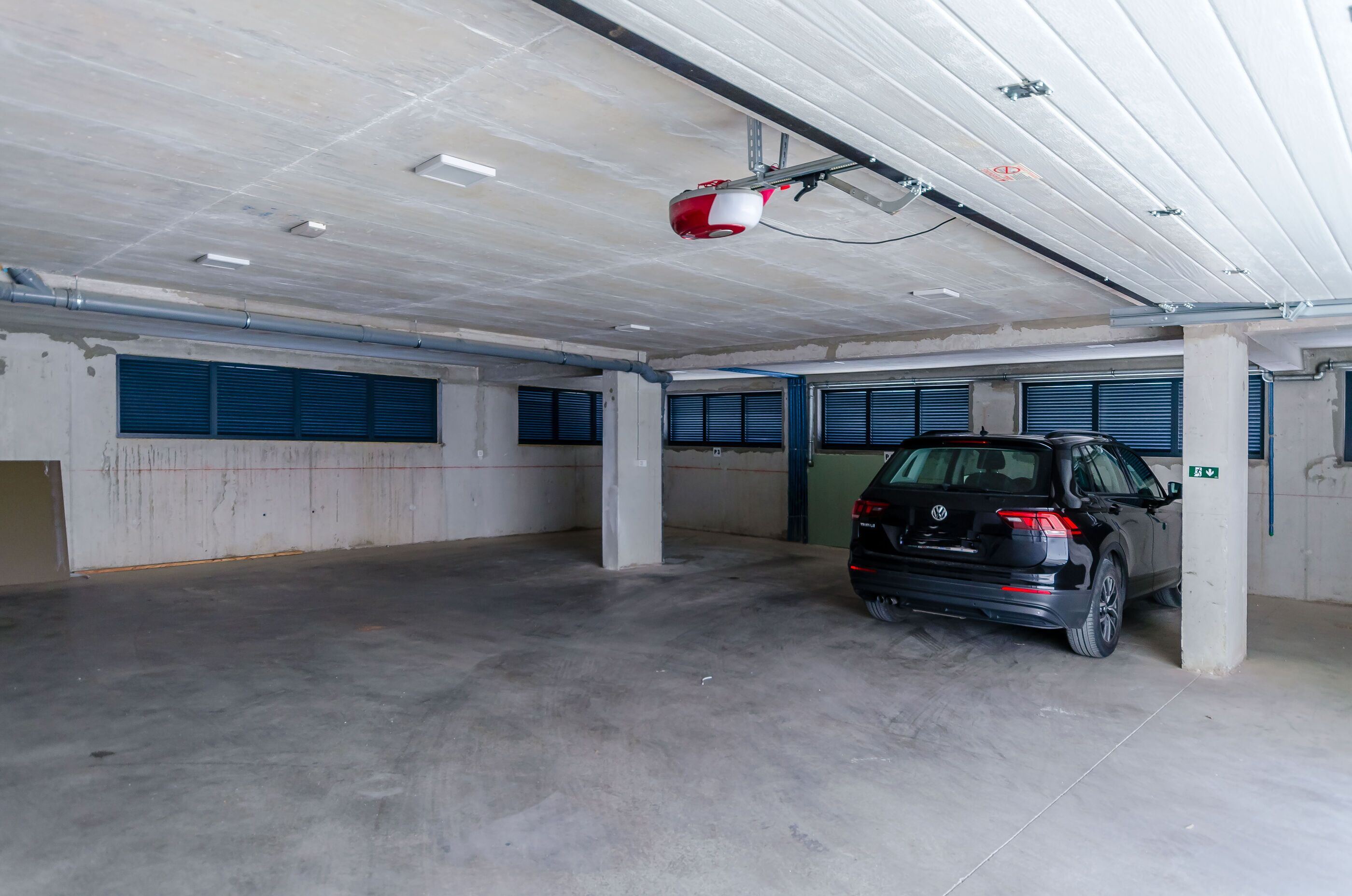 Eine Tiefgarage mit einem schwarzen SUV, das in der Nähe einer Säule geparkt ist, mit Betonböden und blauen Garagentoren.