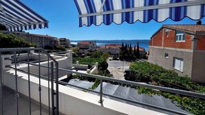 A balcony with a view of a coastal town, featuring buildings with red roofs and a clear blue sky. - Apartments Antonio (Duce)