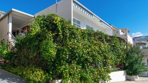 A modern two-story building with a white facade, a balcony, and a lush green ivy-covered wall. - Apartments Antonio (Duce)