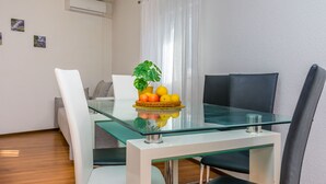 A modern dining area with a glass table, white chairs, and a fruit basket. - Apartments Ivanka (Duce)