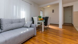 A modern living room with a grey sofa, a dining table with chairs, and a wooden floor. - Apartments Ivanka (Duce)