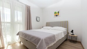 A neatly made bed with a grey blanket, a bedside table with a lamp, and a wall-mounted mirror. - Apartments Ivanka (Duce)