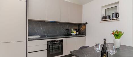 A modern kitchen with a black marble countertop, built-in oven, and a dining area with two wine glasses and a bottle.