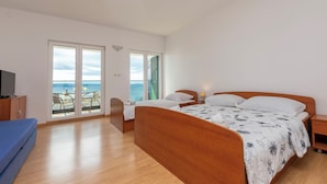 A bedroom with a wooden bed, a TV, a desk, and a balcony with a table and chairs. - Apartments Villa Milas With Pool (Jesenice)