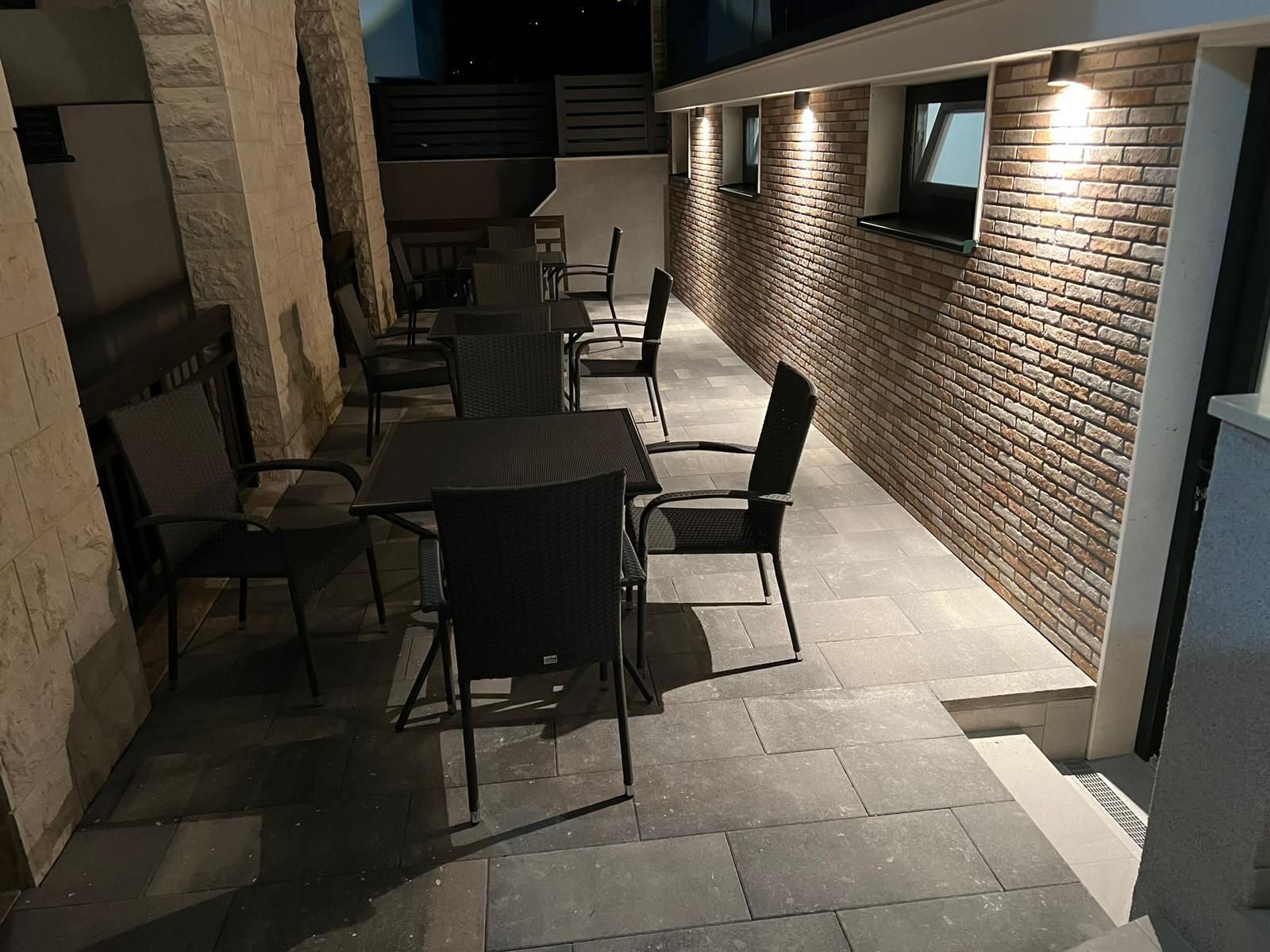 An outdoor patio with a brick wall, tiled flooring, and black metal furniture.
