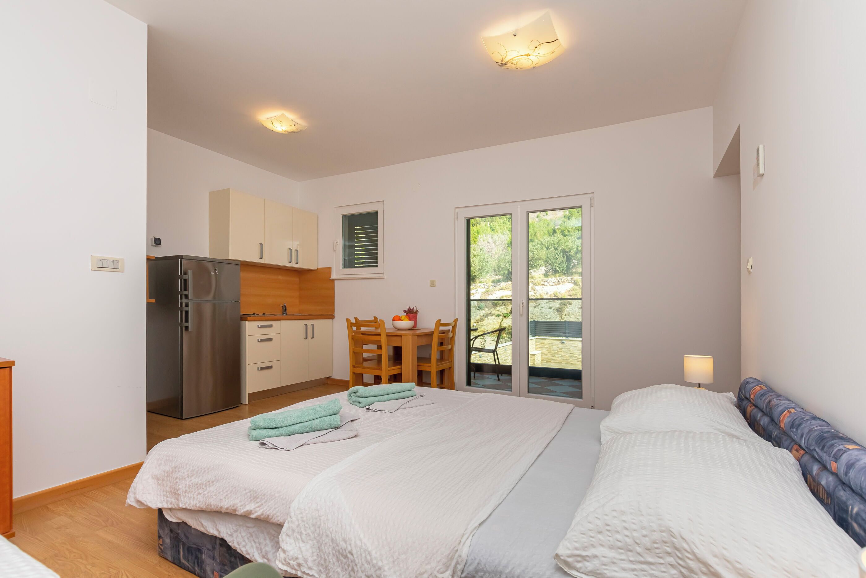 Un dormitorio con cama, una pequeña kitchenette, zona de comedor y puerta corrediza de vidrio al exterior.